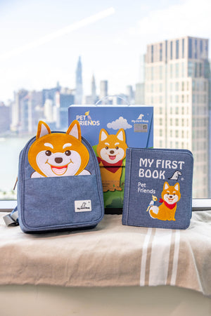 A product shot of the My First Book Pet Friends busy book set against a city skyline, featuring the Montessori-inspired busy book, a waterproof Shiba Inu backpack, and gift-ready packaging—an ideal baby gift.