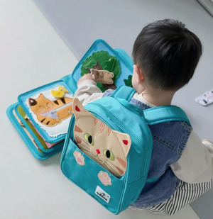 Baby playing with My First Book Lucky Cat busy book with the cat backpack on, engaged in the Montessori inspired play and sensory activities. Makes a great baby gift.