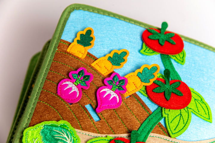 MyFirstBook fabric busy book page with garden scene featuring colorful felt vegetables including carrots, radishes, and tomatoes