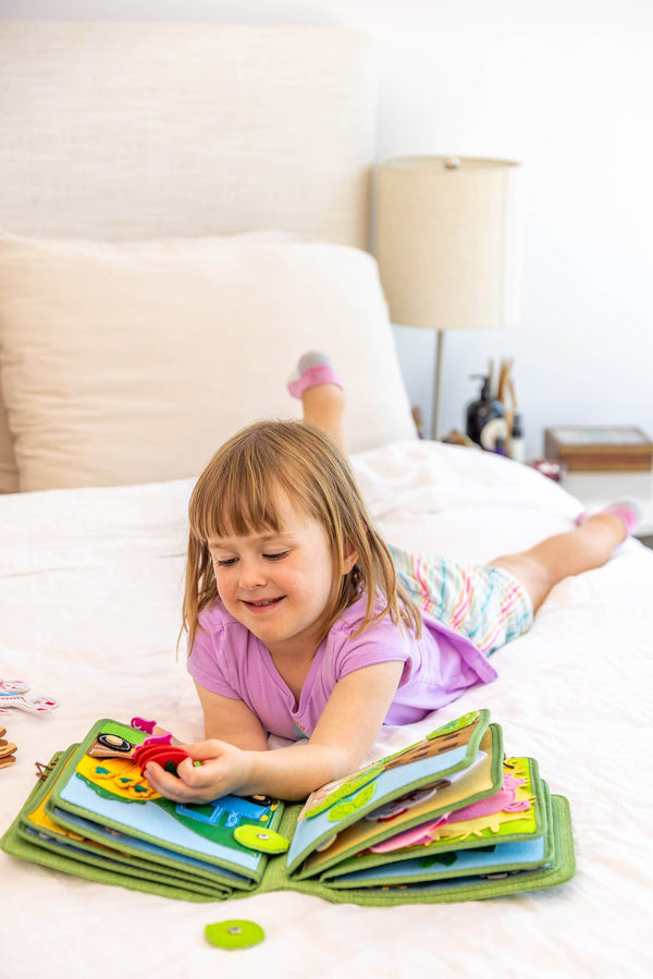 Young girl smiling as she learns and explores with the Montessori sensory play offered by My First Book Busy Farm busy book. Makes a great baby gift.
