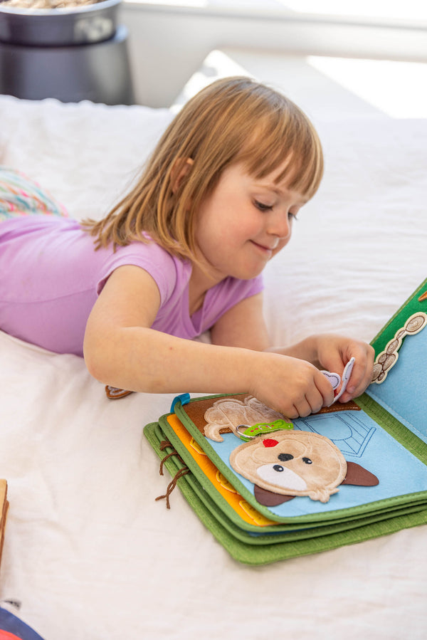 Young girl playing with My First Book Busy Farm busy book, showing she is smiling and having fun with the Montessori style sensory play. Makes a great baby gift.
