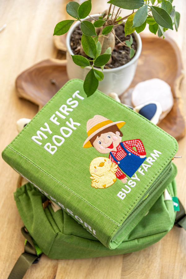 A photo of My First Book Busy Farm busy book sitting on top of the high-quality, waterproof backpack. 
