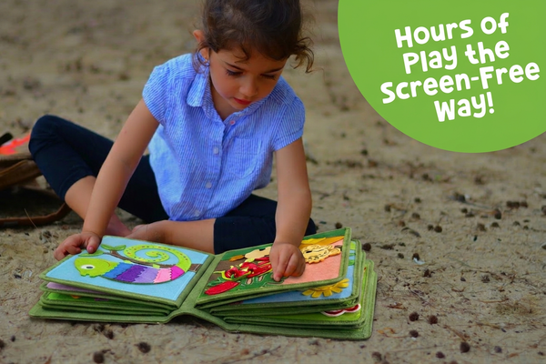 toddler in blue shirt playing with colorful MyFirstBook fabric busy book on ground