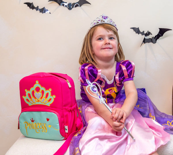 A young girl poses next to her princess backpack, a waterproof backpack included with the My First Book Princess Montessori book. Makes a great baby gift.
