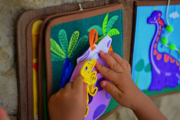 A young child explores sensory skills with Montessori-inspired play in the My First Book Dinosaur busy book. An ideal gift for babies, it sparks curiosity and engagement through interactive dinosaur-themed activities.