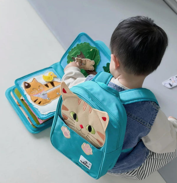 Baby playing with My First Book Lucky Cat busy book with the cat backpack on, engaged in the Montessori inspired play and sensory activities. Makes a great baby gift.
