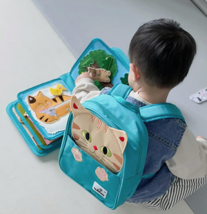 Baby playing with My First Book Lucky Cat busy book with the cat backpack on, engaged in the Montessori inspired play and sensory activities. Makes a great baby gift.
