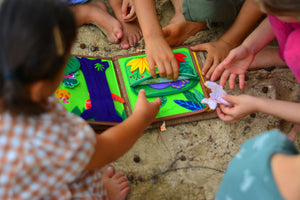 A lively scene with multiple kids gathered on the beach, engrossed in the My First Book Dinosaur busy book. They explore the interactive, dinosaur-themed pages together, building sensory skills through Montessori-inspired play in a fun, outdoor setting.