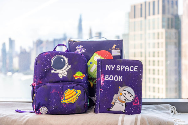 A photo that shows everything included with the My First Book Space, including packaging that makes a perfect baby gift, a busy book inspired by Montessori style sensory play, and a high-quality, waterproof backpack.