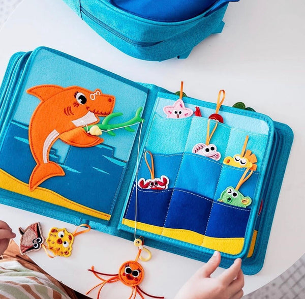 A young child building sensory skills through Montessori inspired play with the fishing game in the Baby Shark busy book. Makes a great baby gift. 